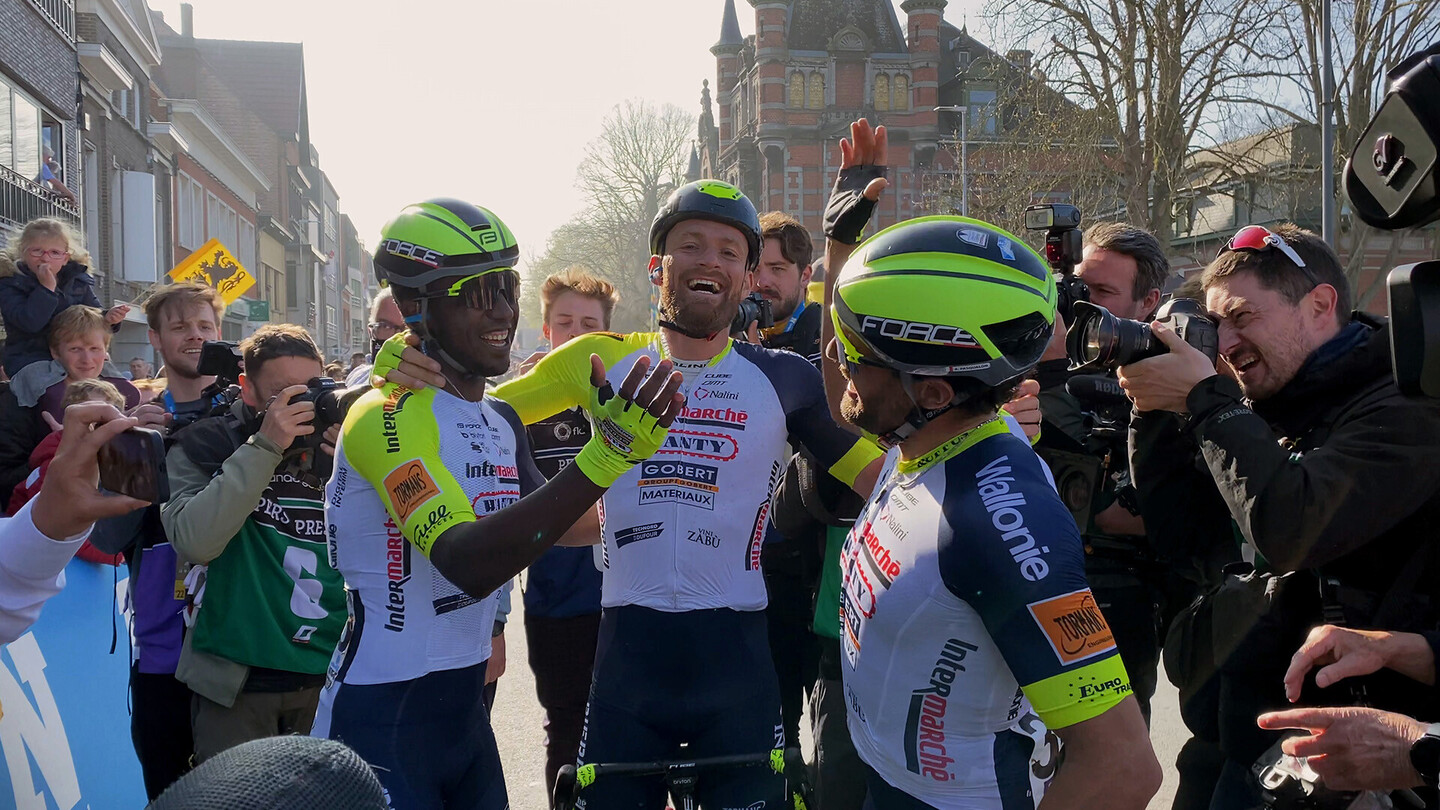 Rennradfahrer feiern an der Ziellinie, umgeben von Fotografen und Fans.