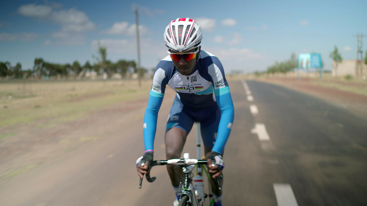 Biniam Girmay fährt auf einem Rennrad auf einer offenen Strasse, trägt ein blau-weisses UCI-Raddress und einen Helm.